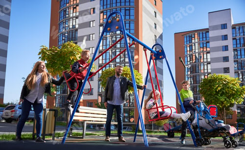 Preview: Happy family - father, mother and children having fun together on playground.