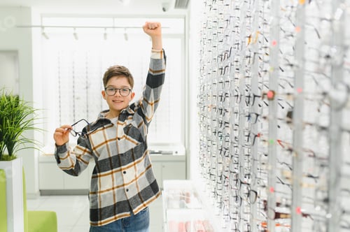 Preview: Young boy celebrating finding new glasses in optical store