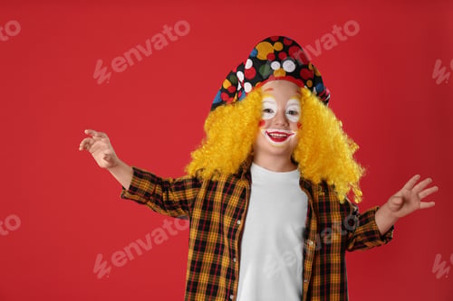 Preview: Funny little boy in clown costume on red background. April fool's day