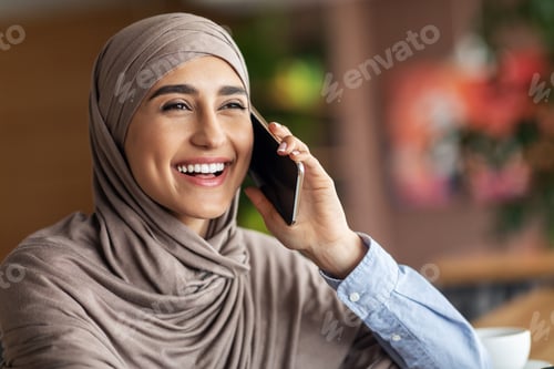 Preview: Laughing muslim girl talking on phone while resting at cafe