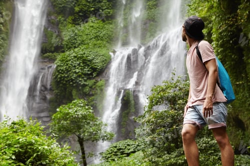 Preview: People, wildlife and adventure concept. Fashionable young adventurer with backpack contemplating wat