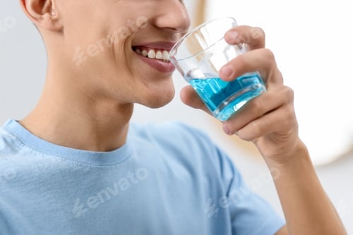 Preview: Young man using mouthwash indoors, closeup view