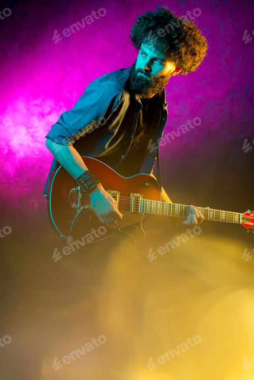 Preview: Young hipster man with curly hair with red guitar in neon lights.