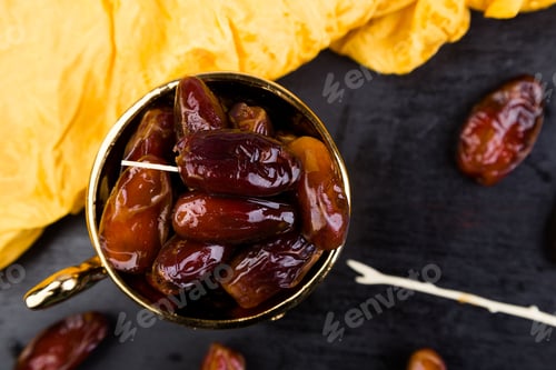 Preview: Dry fruit dates in golden cup near slate black heart. Copy space.