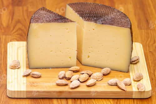 Preview: Selective focus shot of unpeeled almonds and manchego cheese on a wooden board