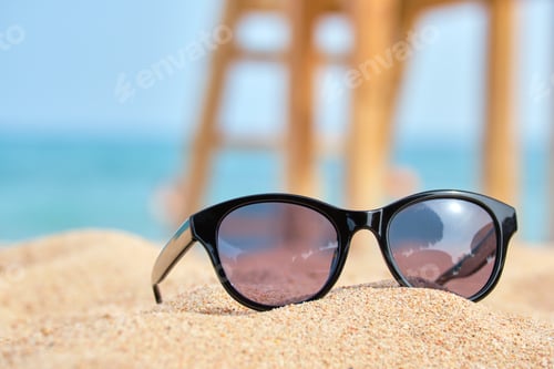 Preview: Closeup of black protective sunglasses on sandy beach at tropical seaside