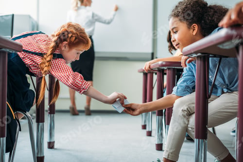 Preview: schoolgirls passing message in class on lesson