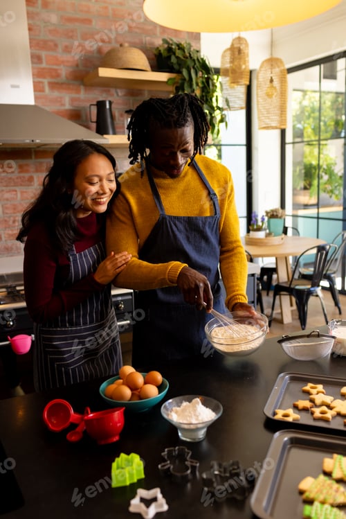 Preview: Happy diverse couple baking christmas cookies mixing dough in kitchen, copy space