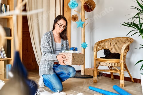 Preview: Woman wrapping christmas gifts in craft recycled paper in the room with alternative christmas tree