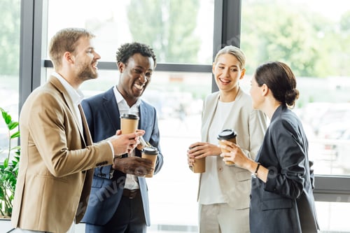 Preview: four multiethnic colleagues holding disposable cups of coffee and smiling in office