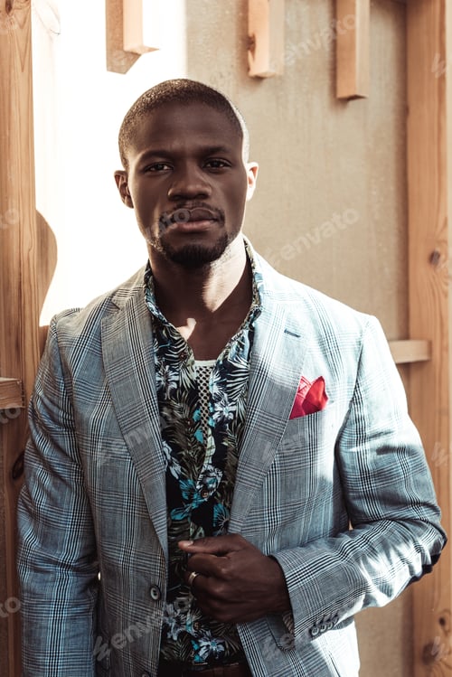 Preview: Handsome african american man in stylish suit, leaning on wooden wall and looking at camera