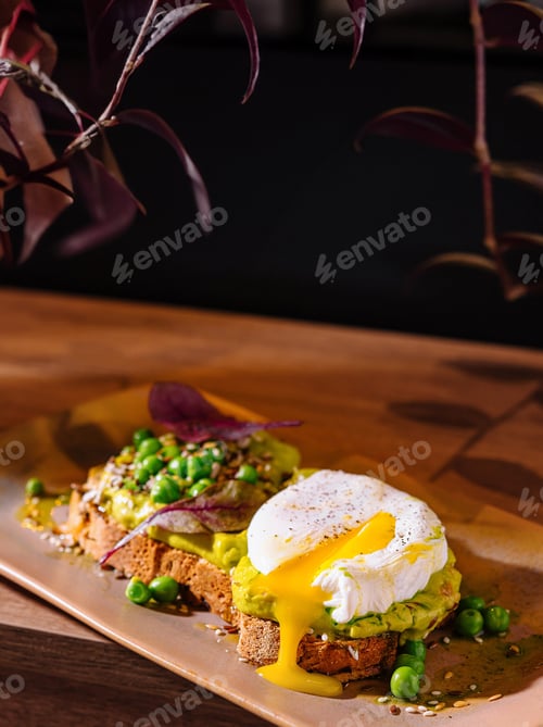 Preview: Delicious poached egg toasts with avocado and peas on wooden table