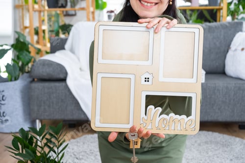 Preview: Happy woman in house holds in hands photo frame with figure at home template and key in interior. Dr