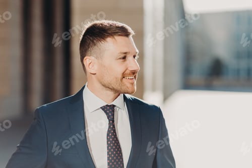 Preview: Cheerful unshaven male looks aside with joyful expression, wears formal clothes.