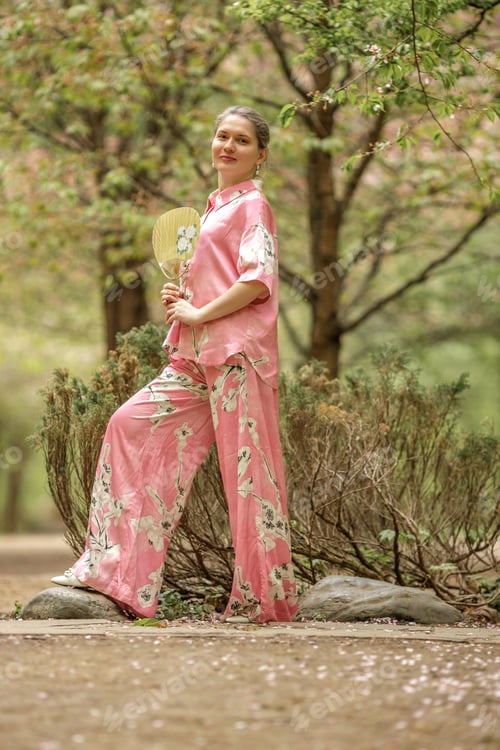 Preview: Young woman in pink national costume of Japan, walking in a garden with blooming sakura