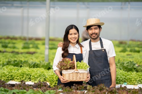 Preview: Happy ypung Asian couple smailing at hte camera while standing in a hydroponics farm.