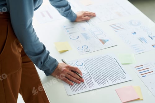 Preview: Hand of young female employee with pen over contract paper on desk