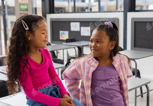 Preview: Two biracial girls are sharing a moment in a school classroom setting