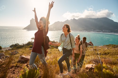 Preview: Young adult friends hiking single file uphill celebrate reaching a summit, full length, side view
