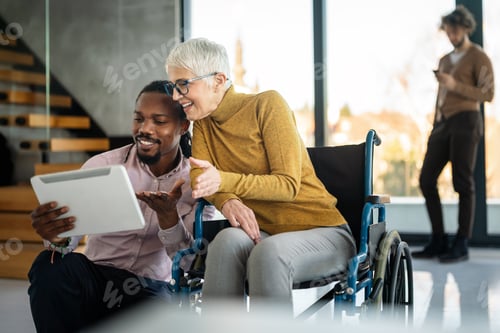 Preview: Disabled woman in wheelchair looking at computer, discussing startup project with interracial team