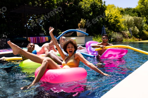 Preview: Happy diverse group of friends having pool party, using swim rings in swimming pool in garden