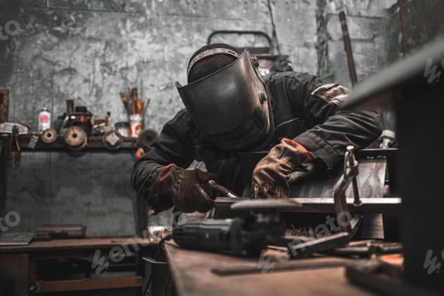 Preview: Worker in a welder mask works in a workshop for welding iron. Man makes iron products.