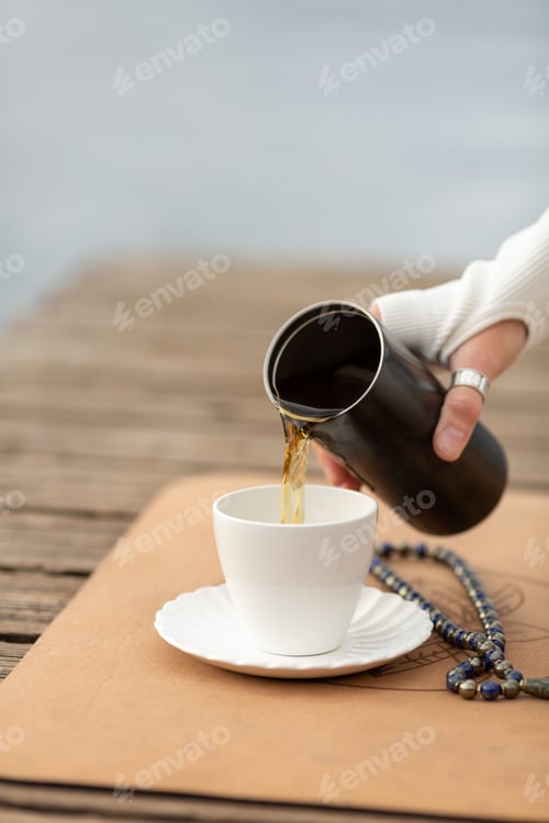 Preview: A woman after yoga practice pours herbal tea from a thermos into a white cup, Malas beads