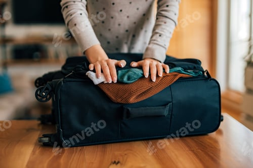 Preview: Woman packing a luggage for travel, close-up.