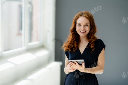 Portrait of content redheaded businesswoman with digital tablet in a loft