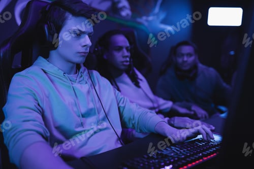 Preview: Focused man in headphones playing video game near blurred multiethnic friends in cyber club