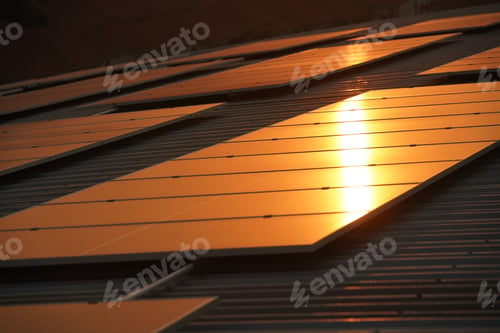 Preview: Solar panels on the meadow, sunset reflected on solar panel on rooftop. Green energy concept