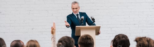 Preview: panoramic shot of happy speaker pointing with hand at journalist with raised hand