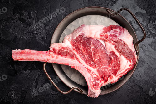 Preview: Raw tomahawk steak with marbling, fresh rib eye with bone. black background. top view