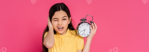 Preview: schoolgirl looking at camera, winking, holding alarm clock isolated on pink, back to school, banner