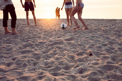 Preview: Young men, young woman and teenage girl (16-17) playing soccer on sand at sunset