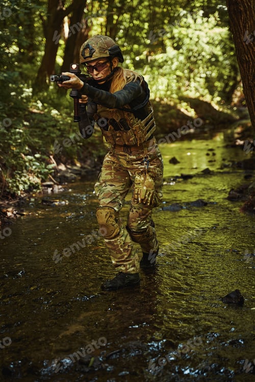 Preview: Woman in helmet standing in forest and holding gun in hands