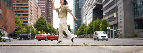 Preview: Portrait of asian happy girl jumping and dancing in city centre, posing on streets, express joy and