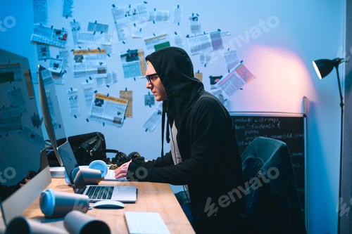 Preview: side view of hooded young hacker working with computer