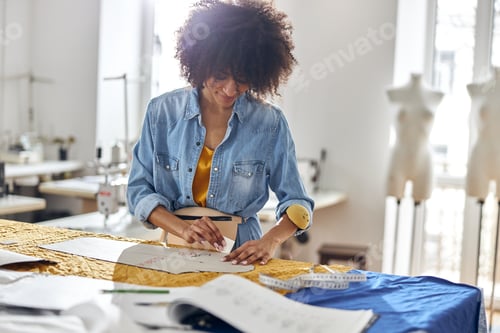 Preview: Professional African-American dressmaker draws pattern on fabric working at cutting table