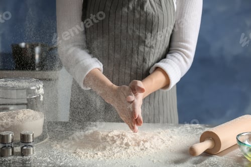 Preview: Woman sprinkling flour over table in kitchen