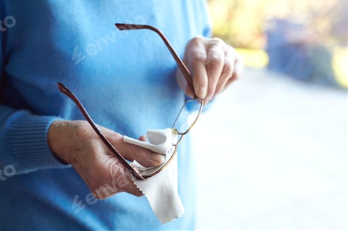 Preview: Senior woman cleaning eyeglasses with cloth, mid section