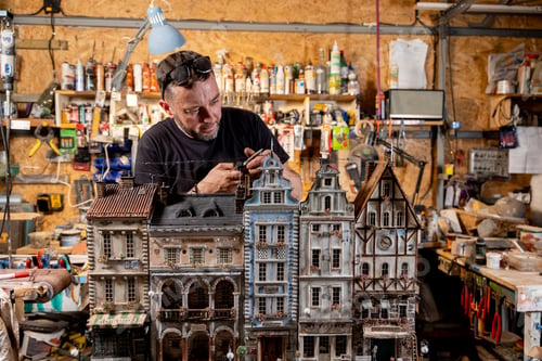 Preview: Modeller man working at scale model of miniature building in his workshop full of tools