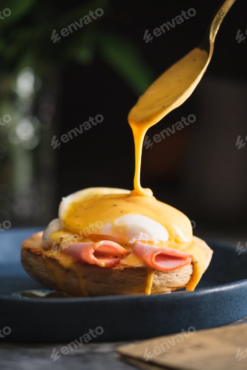 Preview: egg Benedict with hollandaise sauce on dark blue plate on table in kitchen