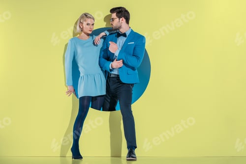 Preview: attractive stylish couple stepping through aperture on yellow