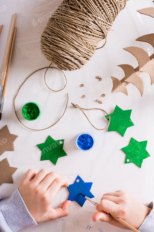 Preview: A child paints a gouache star from cardboard for DIY Christmas decorations. Top and vertical view.