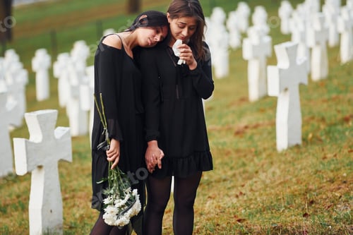 Preview: Two young women in black clothes visiting cemetery with many white crosses