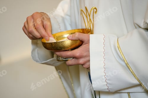Preview: Priest wearing a white alb with golden ornaments, holding a golden chalice with consecrated hosts