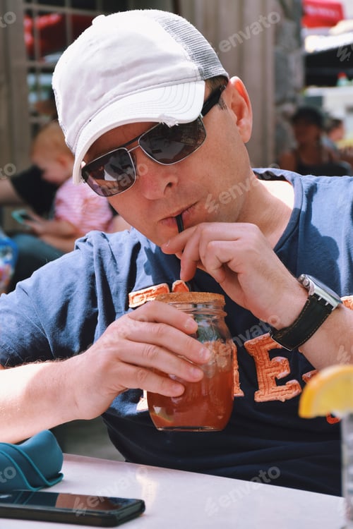 Preview: Man is sipping Caesar cocktail through a straw in an outdoor restaurant