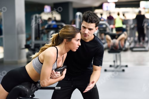 Preview: Personal trainer helping young woman lift weights