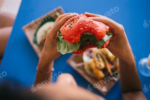 Preview: Female customer eating tasty hearty American burger with tomato bread rolls and vegan meat